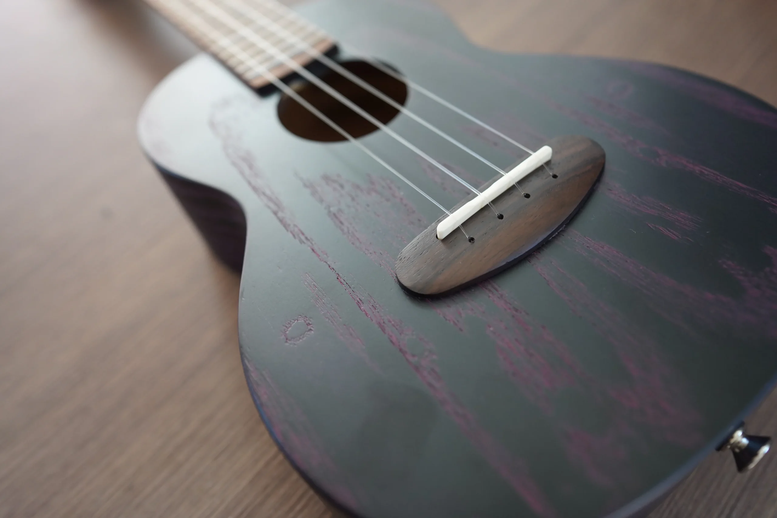 Close-up of the Flight DUC 400 Ash Purple ukulele bridge, saddle, and ash wood grain on the soundboard.
